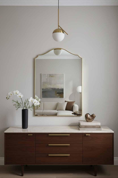 Brass framed arched wall mirror above modern dresser with white orchid flowers, books, and contemporary décor