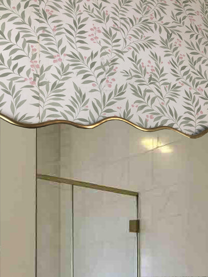 Close-up of brass-framed mirror with floral wallpaper background.