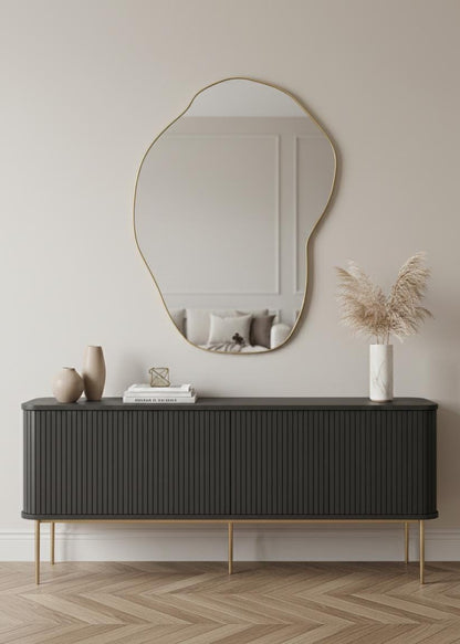 Sculptural irregular brass wall mirror above modern black sideboard