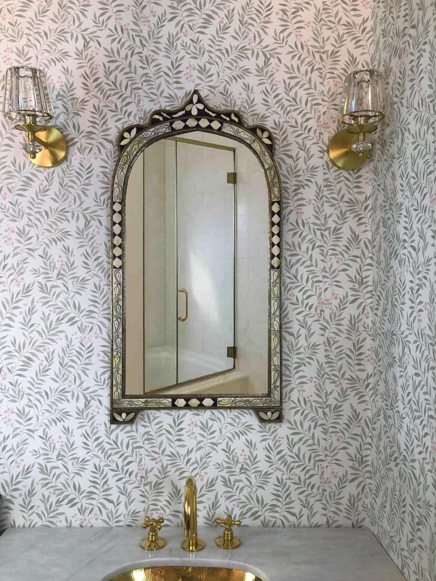 Arched bone inlay mirror above brass sink.