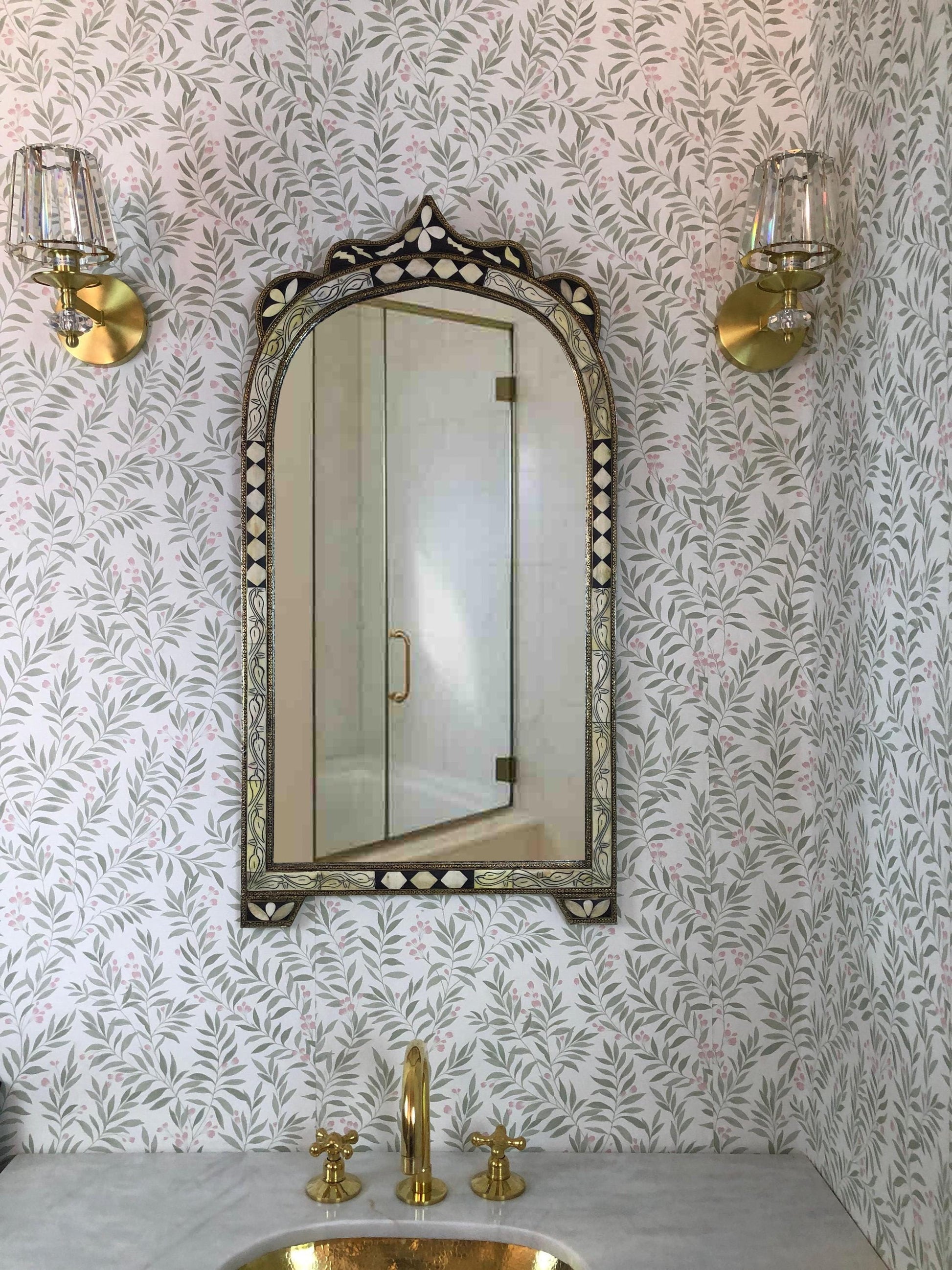 Arched bone inlay mirror above brass sink.
