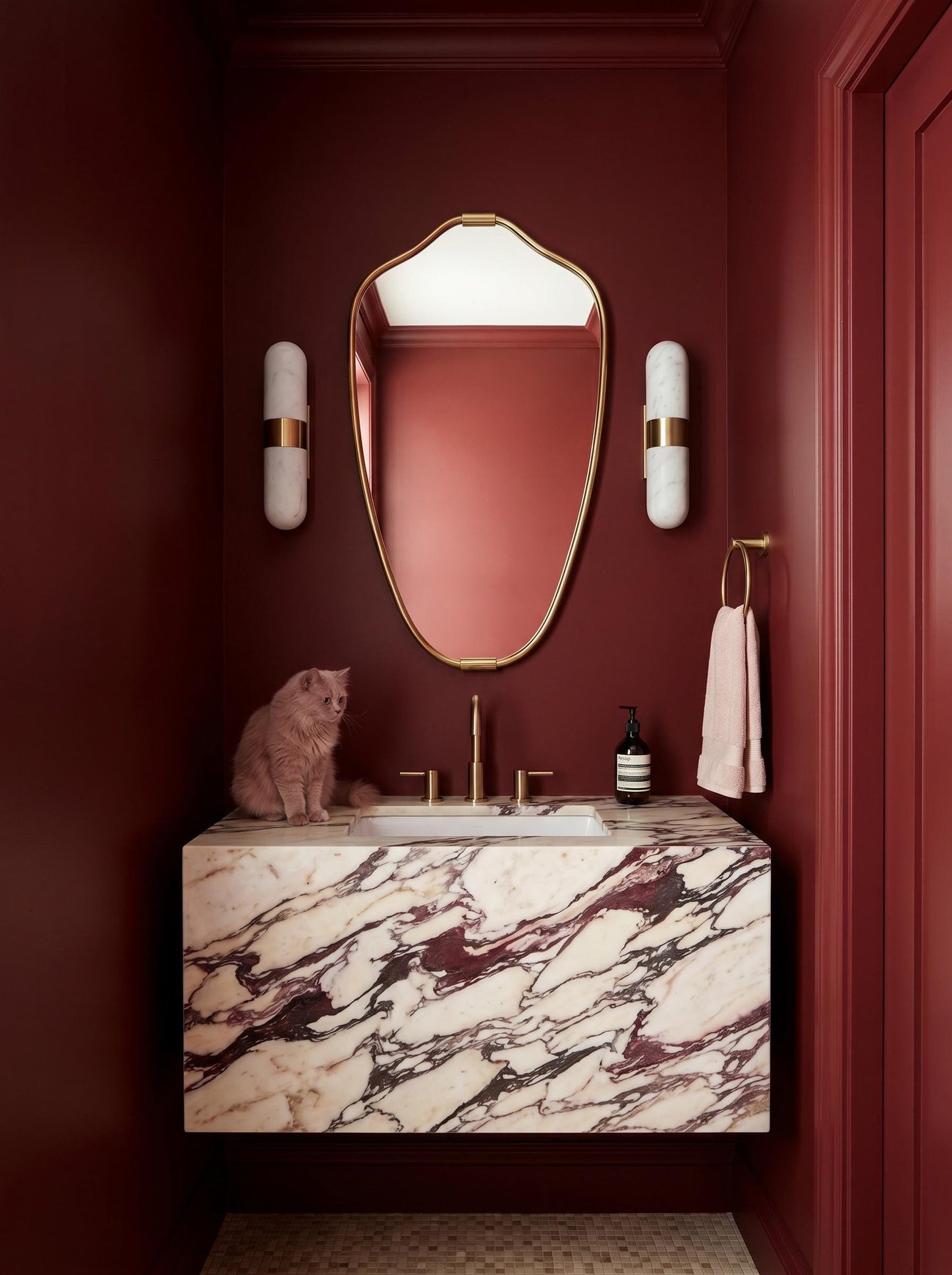 Sculptural brass mirror in red luxury bathroom with marble sink