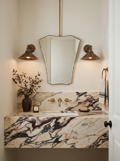 Geometric suspended brass mirror above marble vanity