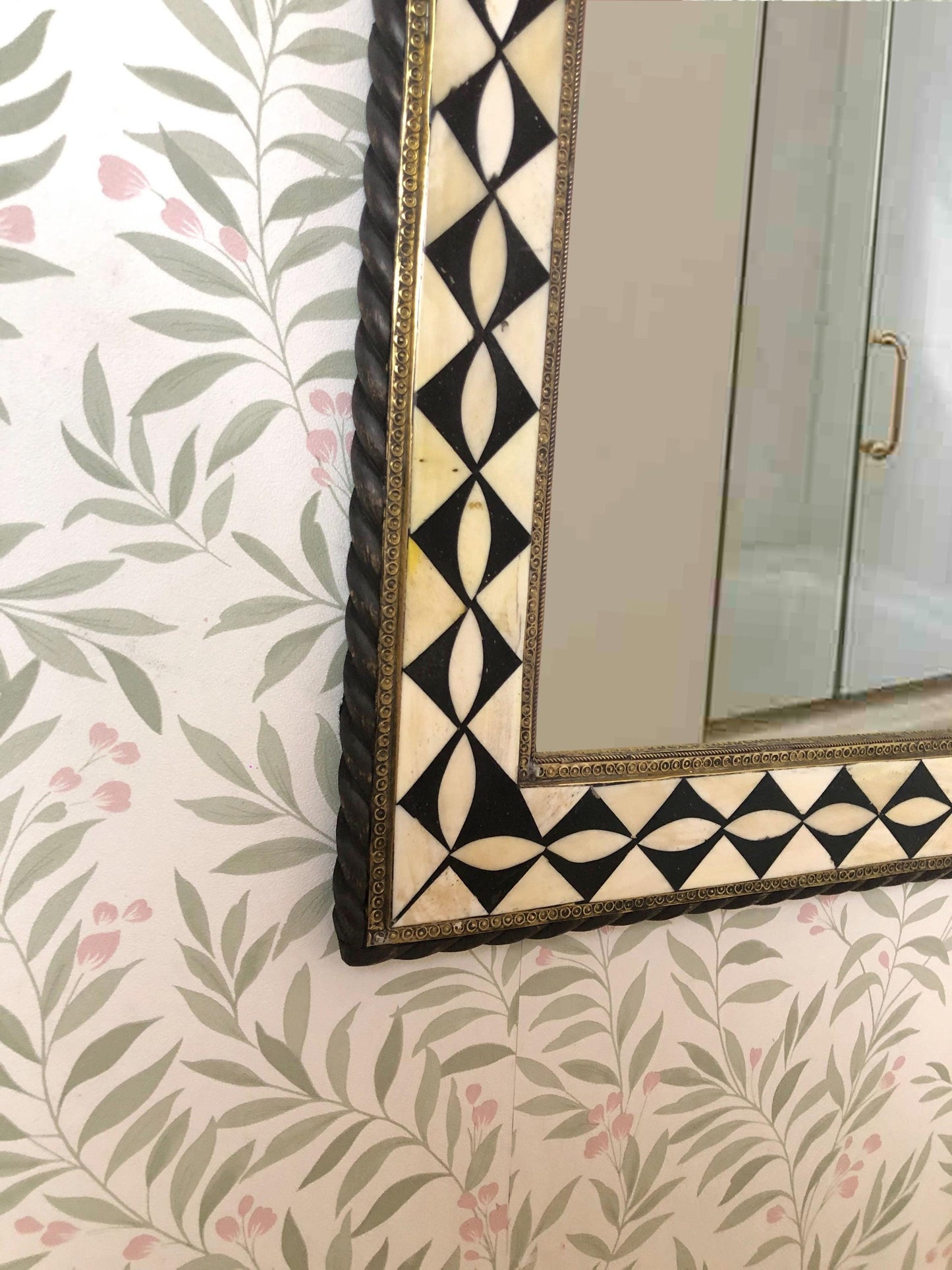 Lower corner of mirror with decorative frame and floral patterned wall.