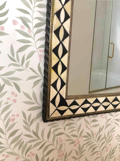 Lower corner of mirror with decorative frame and floral patterned wall.