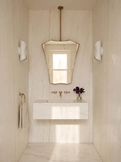 Sculptural brass ceiling mirror in minimalist bathroom