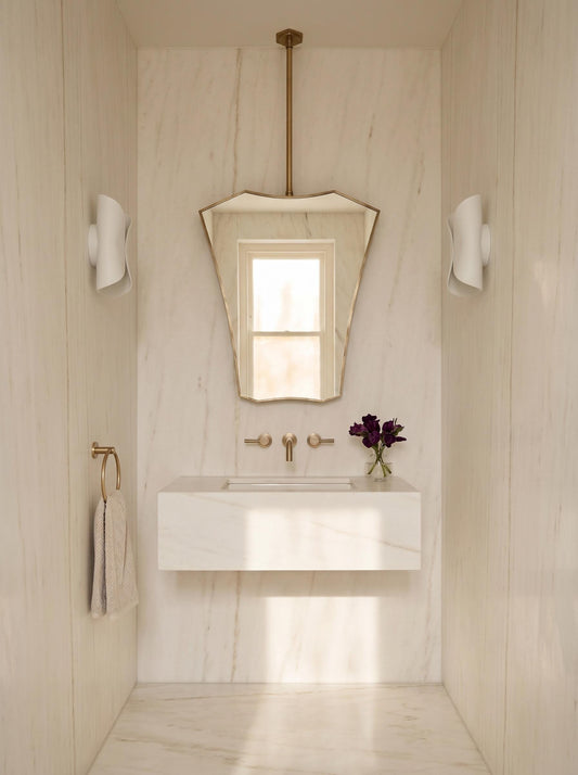 Sculptural brass ceiling mirror in minimalist bathroom
